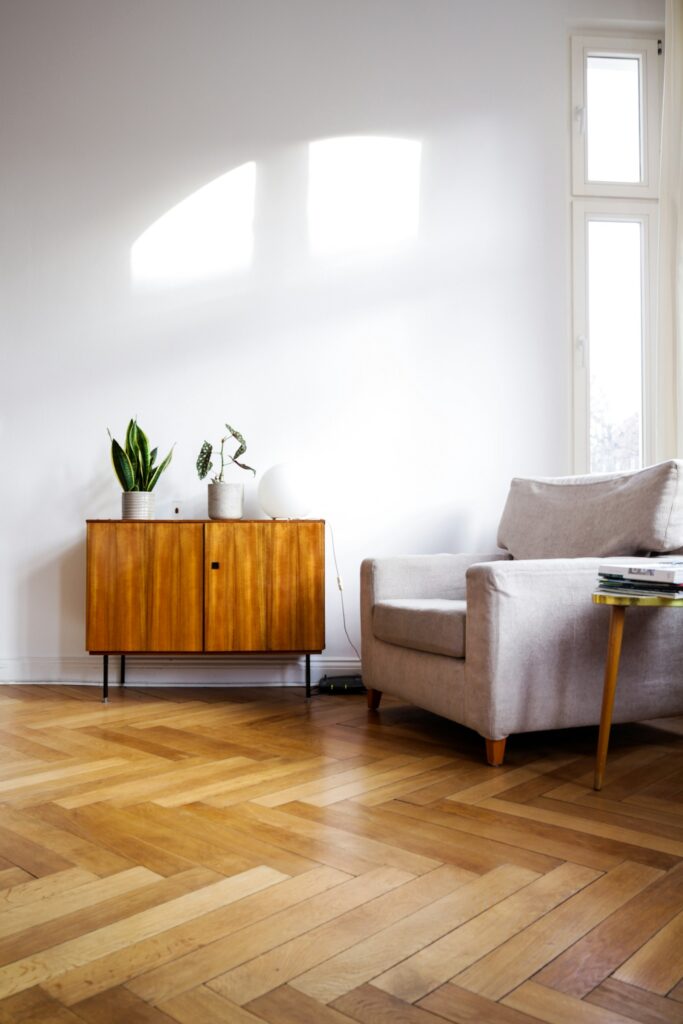 Salón luminoso con suelo de madera, aparador y sillón