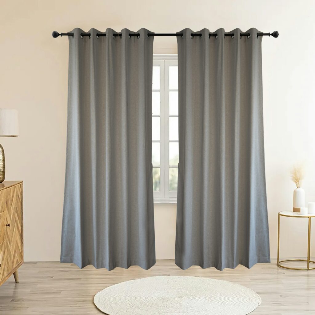 Dos cortinas grises opacas con ollaos colgadas de una barra delante de una ventana